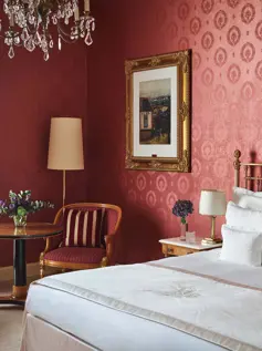 Hotelzimmer mit dunkelroter Seidentapete und Messingbett