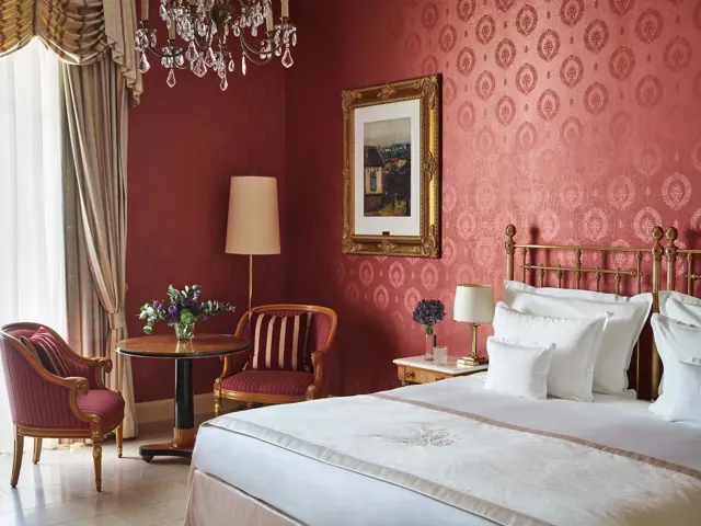 Hotelzimmer mit dunkelroter Seidentapete und Messingbett