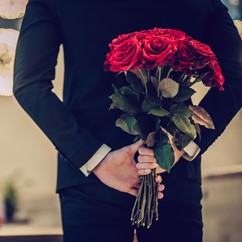 Mann überrascht seine Partnerin mit einem Strauss roter Rosen